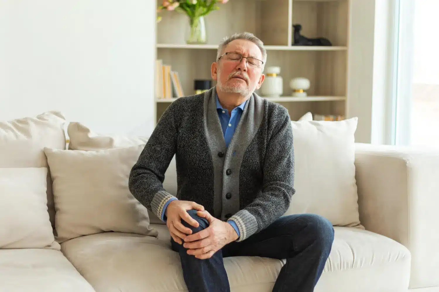 Man experiencing knee discomfort while sitting on a sofa