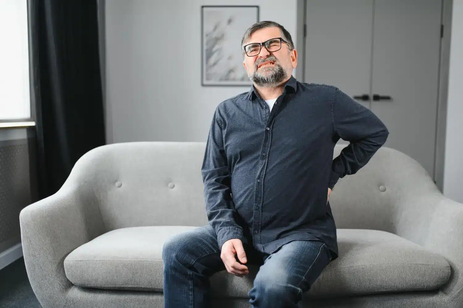 Man experiencing lower back pain while sitting on a sofa