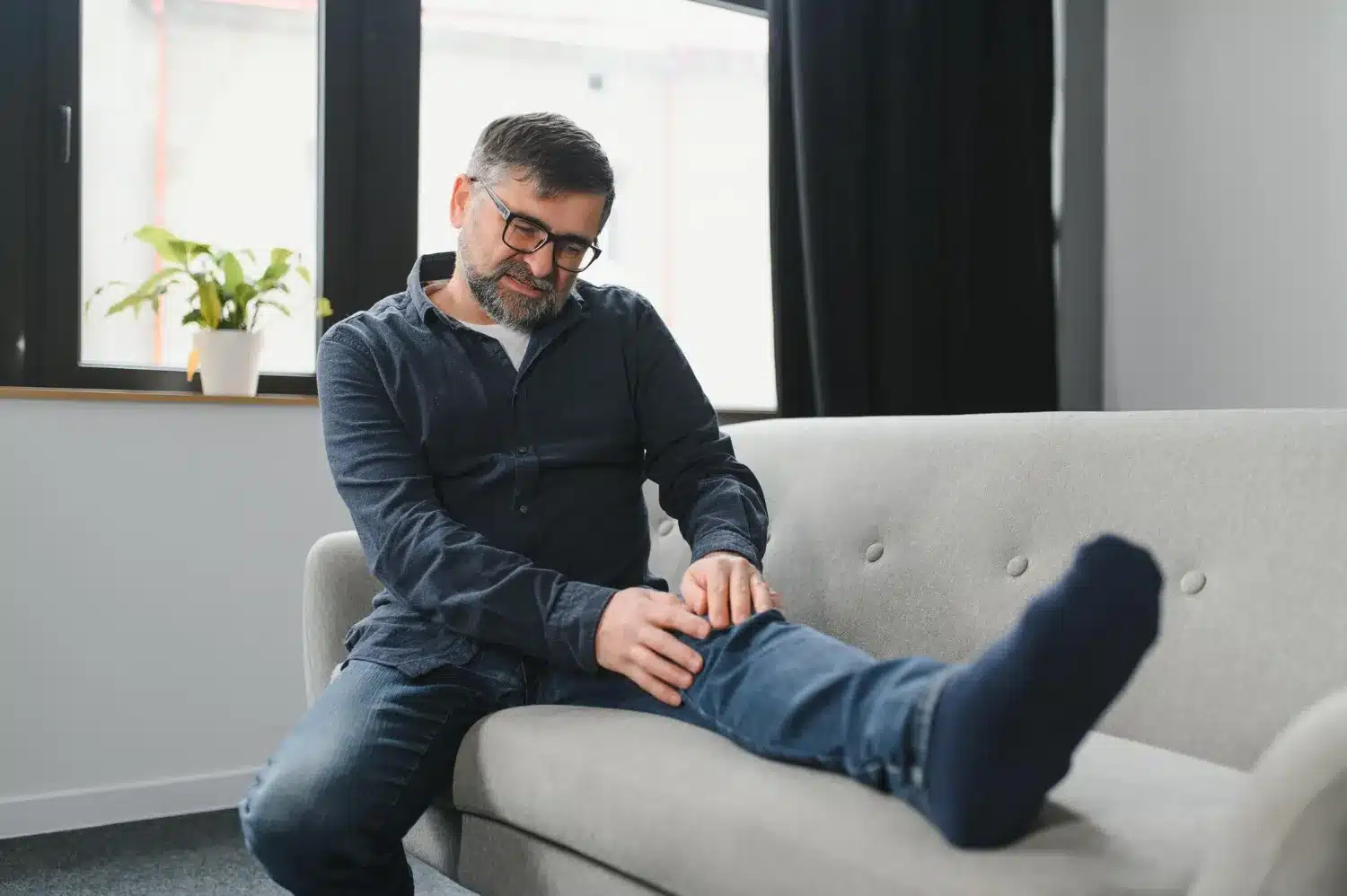Man experiencing knee pain while sitting on a sofa