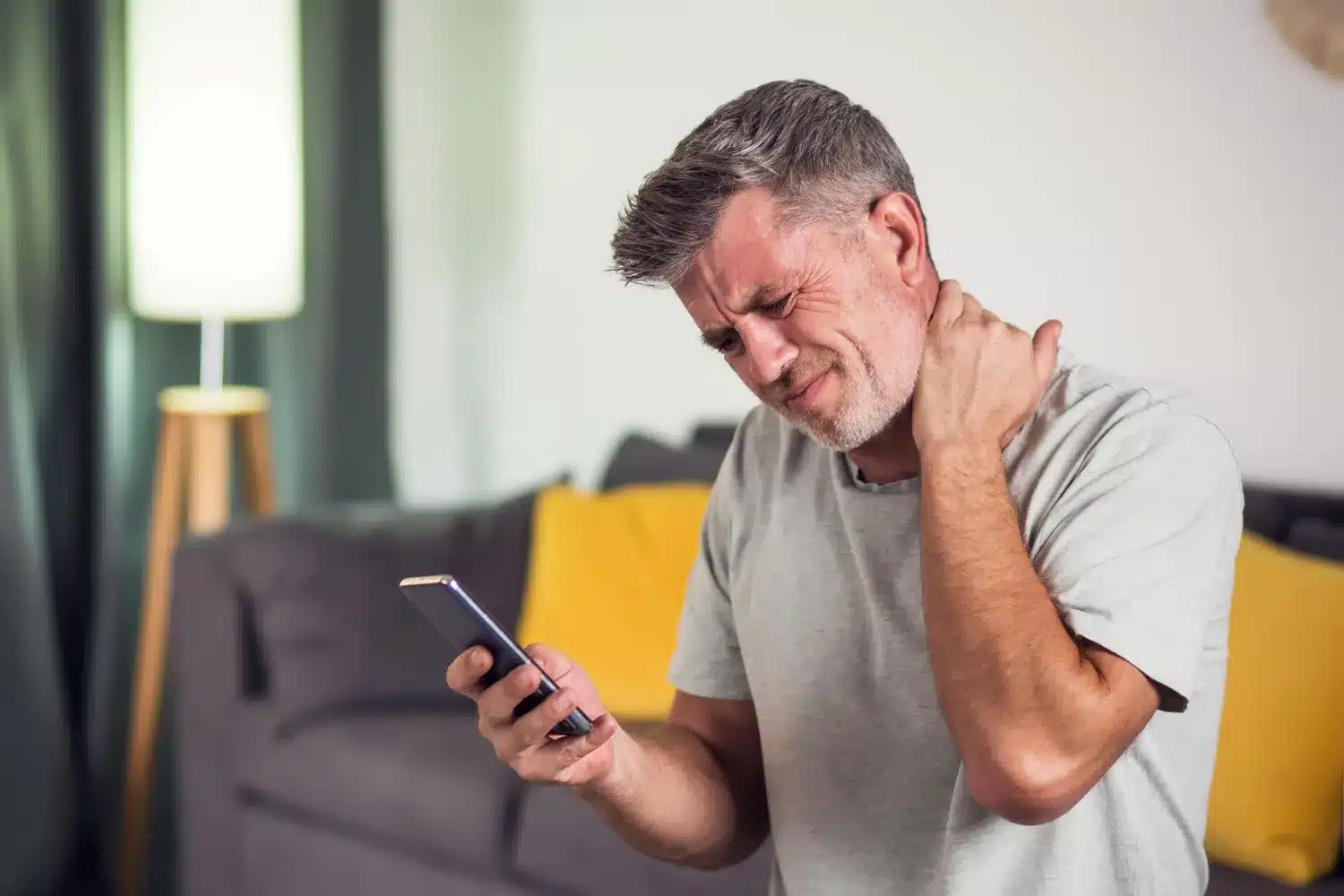 Man holding his neck while using a smartphone