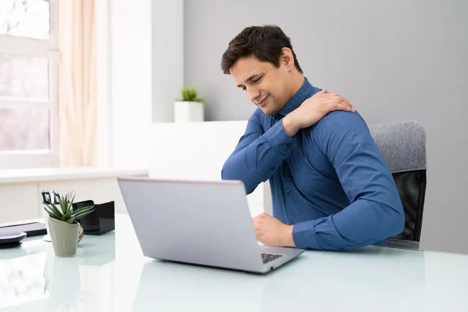 Man experiencing shoulder pain while working at a laptop
